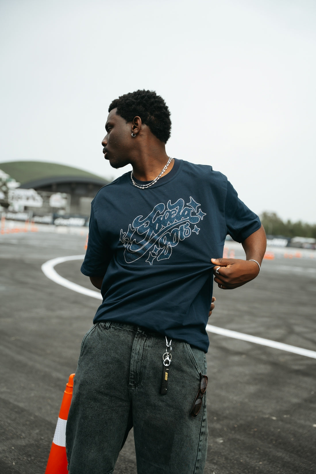 Young man stands on asphalt, adjusting his dark graphic t-shirt.