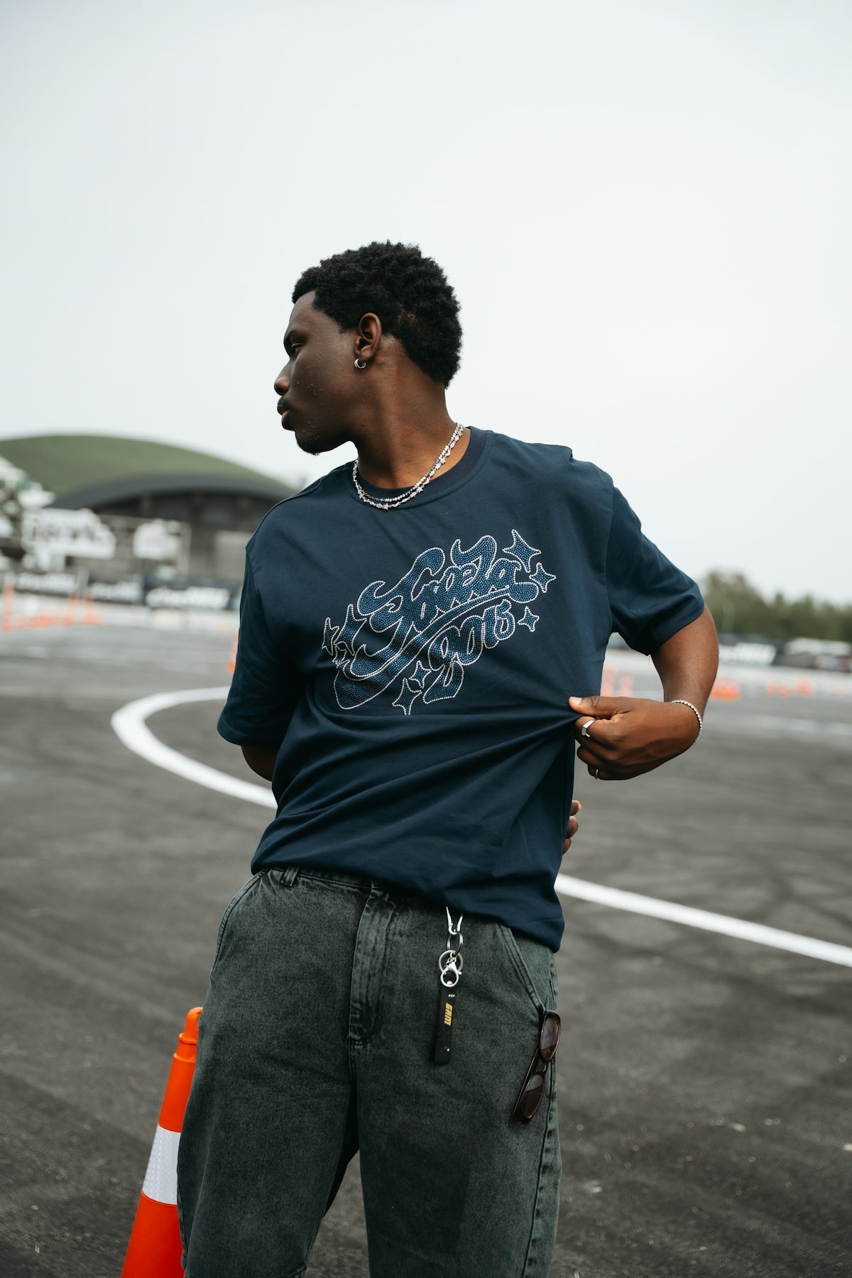 Young man stands on asphalt, adjusting his dark graphic t-shirt.