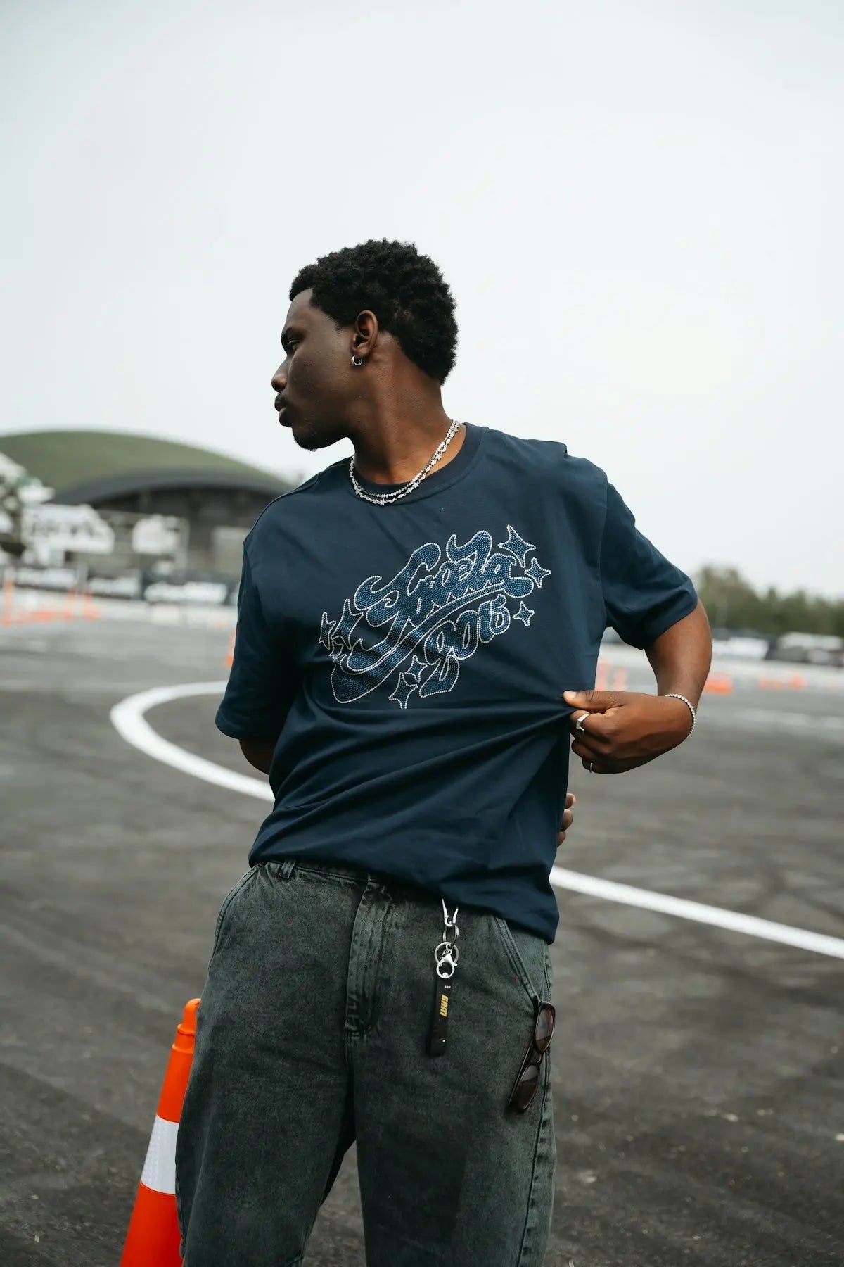 Young man stands on asphalt, adjusting his dark graphic t-shirt.